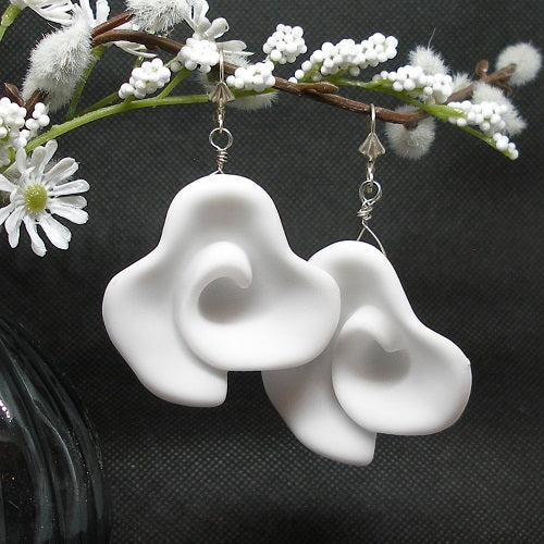 White floral-shaped earrings on a dark background with decorative white flowers.