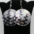 Round earrings with black and white pattern on a black stand.