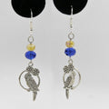 Pair of silver parrot-shaped earrings with blue and yellow beads on a gray background.