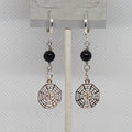 Pair of earrings with black beads and geometric silver charms on a gray card.
