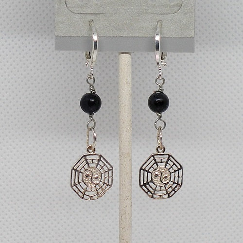 Pair of earrings with black beads and geometric silver charms on a gray card.
