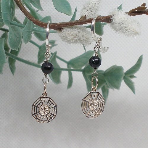 Silver earrings with black beads hanging from a branch with leaves and flowers.