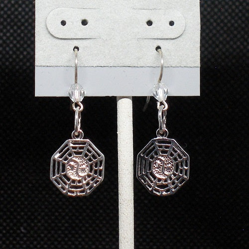 Silver earrings with geometric design on a gray stand against a black background