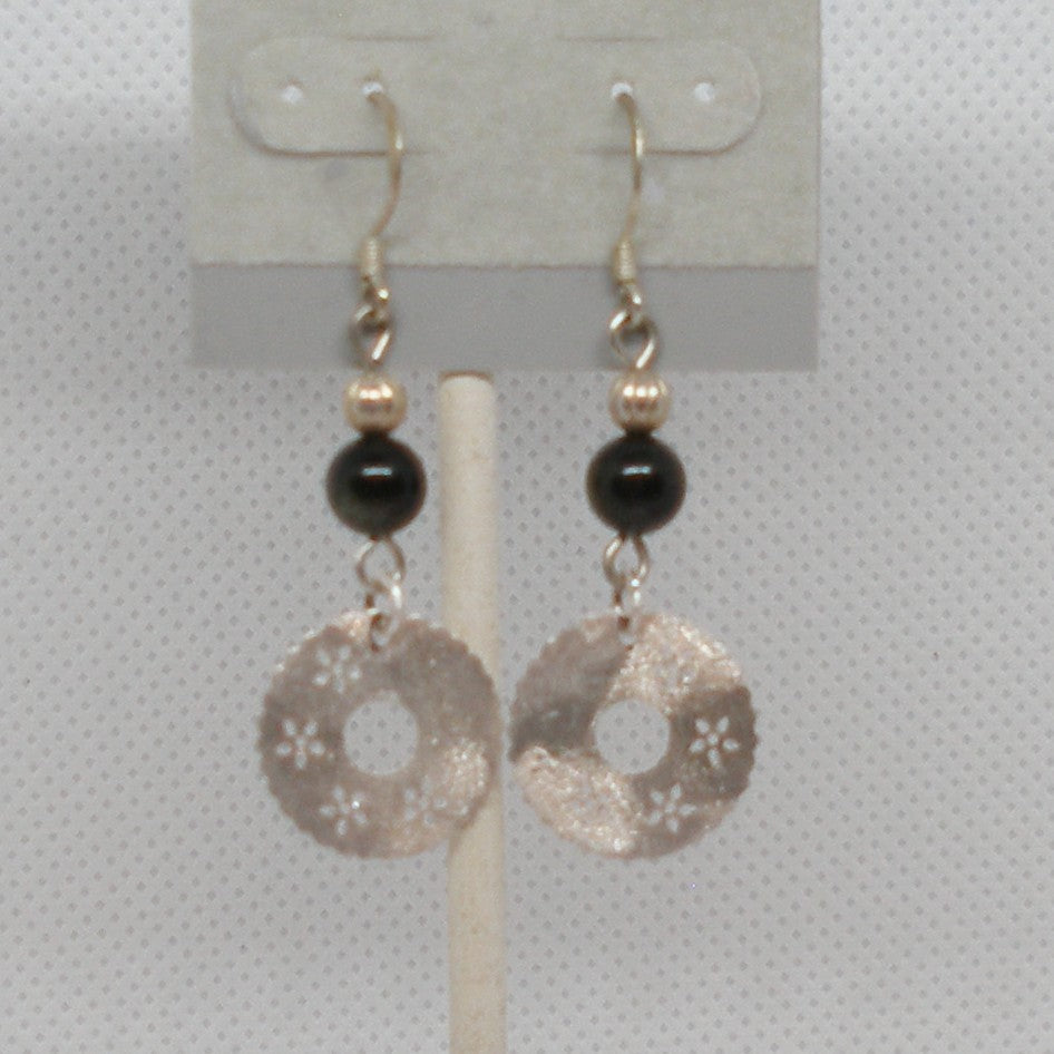 Pair of earrings with black beads and silver circular pendants on a gray background