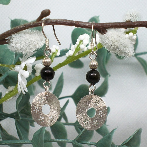 Pair of silver and black beaded earrings hanging on a branch with white flowers.