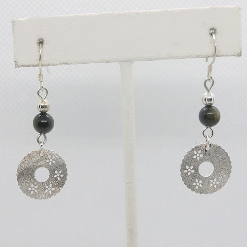 Pair of earrings with silver circular designs and black beads on a white card.