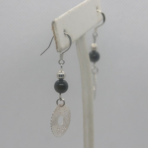 Silver earrings with a central black bead on a white stand against a light gray background