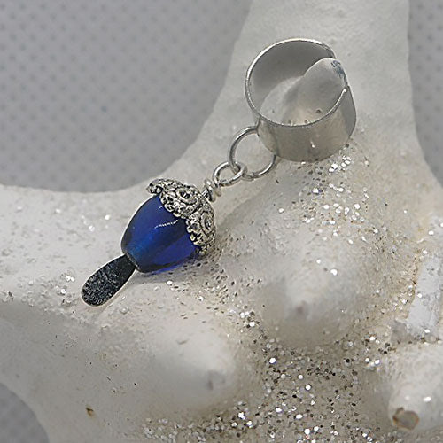 Silver ear cuff with a blue teardrop-shaped stone on a textured white surface