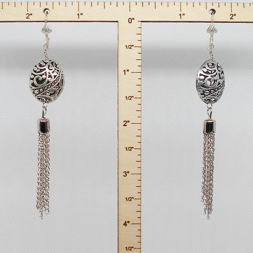 Silver tassel earrings with decorative elements on a ruler for scale.