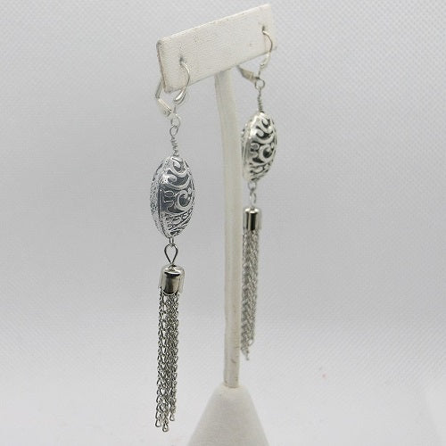 Silver earrings with intricate designs on a white stand against a light gray background