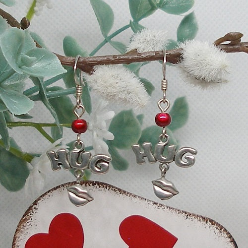 Silver 'HUG' earrings with red beads on a decorative heart and branch background