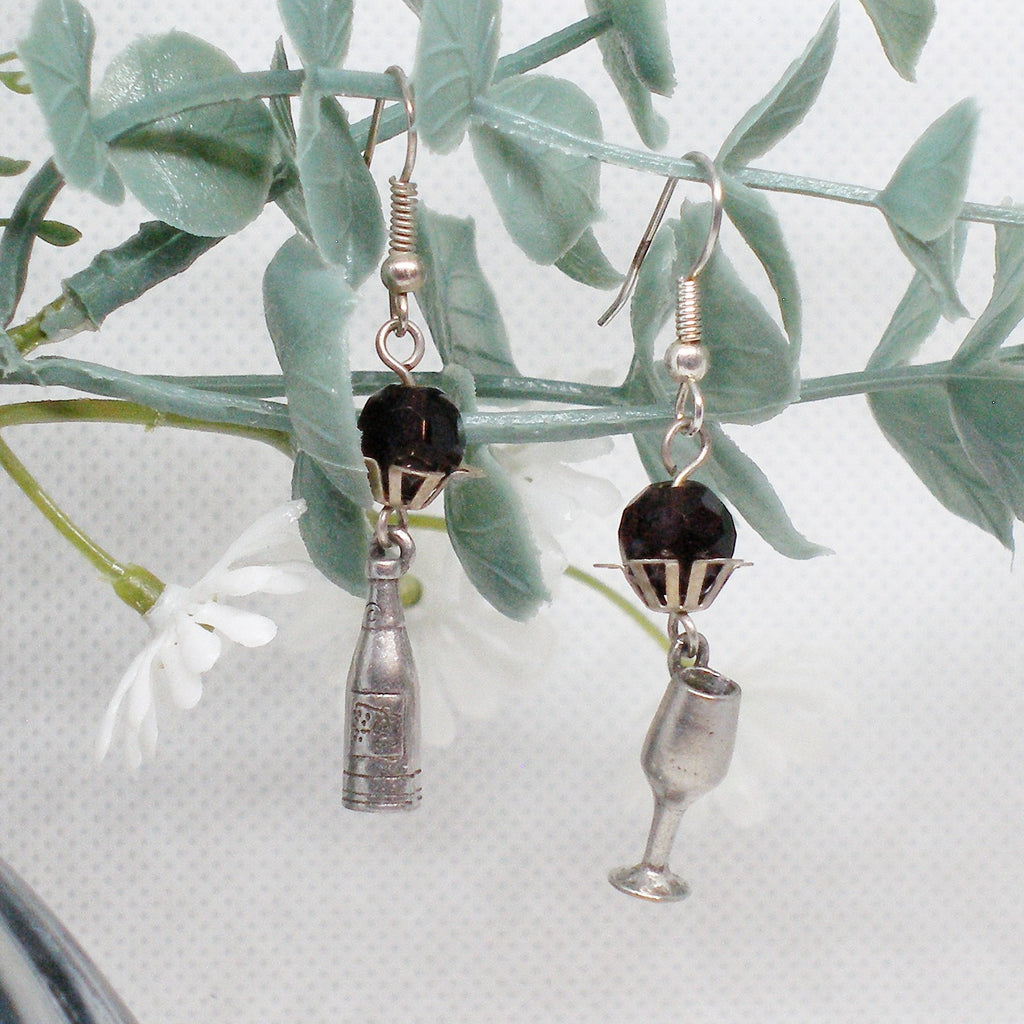 Pair of earrings with bottle and glass charms on a leafy branch.
