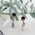 Pair of earrings with bottle and glass charms on a leafy branch.