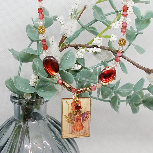 Necklace with a pendant featuring a fairy design, displayed on a branch with green leaves and white flowers.