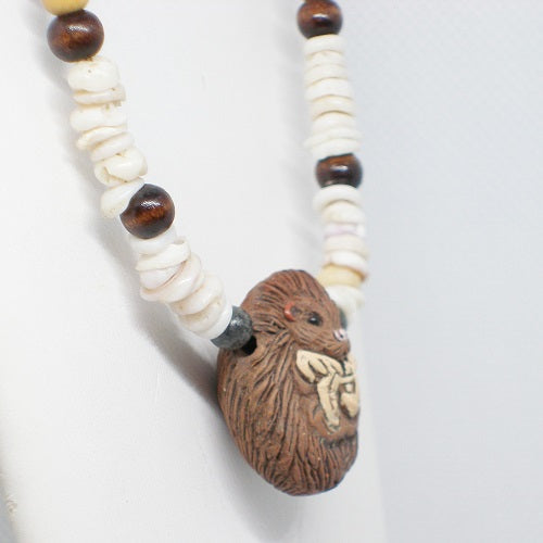 Necklace with clay hedgehog pendant and wood and shell beads on a light gray background