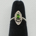 Silver ring with a green gemstone on a black velvet stand against a gray background