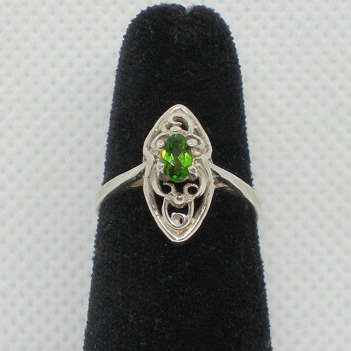 Silver ring with a green gemstone on a black velvet stand against a gray background