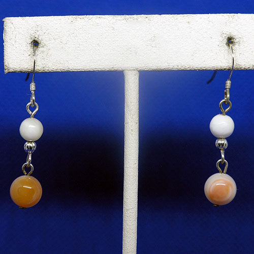 Pair of earrings with white and orange beads on a white stand against a blue background