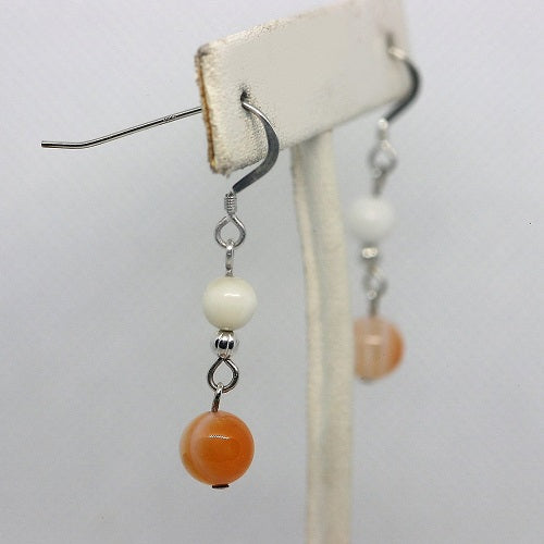 Pair of earrings with orange and white beads on a white background