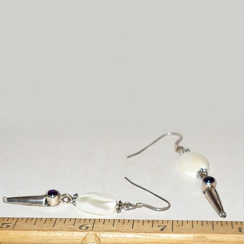 Pair of earrings with mother of pearl, amethyst and silver accents on a white background with a ruler for scale.