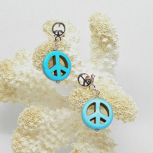 Turquoise peace sign earrings on a piece of coral.