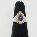 Silver ring with a purple gemstone on a black velvet stand against a white background