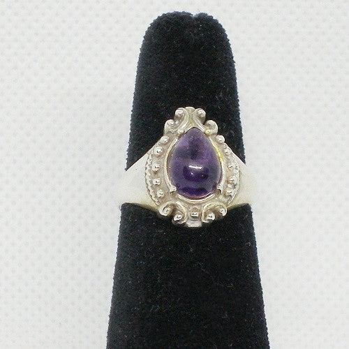 Silver ring with a purple gemstone on a black velvet stand against a white background