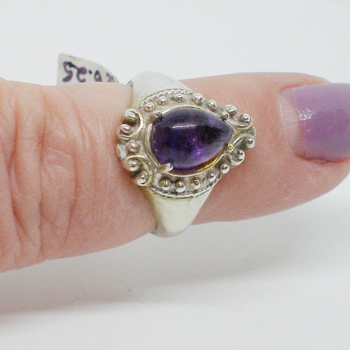 Silver ring with a purple gemstone on a finger against a white background