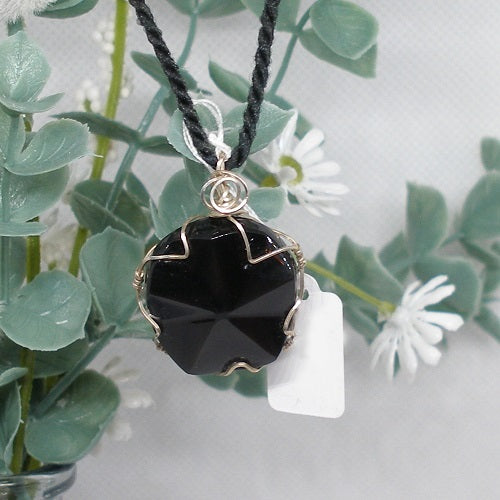 Black stone pendant necklace with silver wire wrapping on a white background with green leaves.