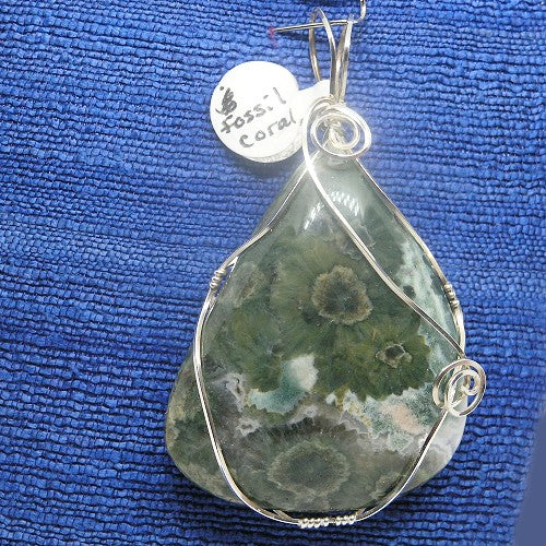 Teardrop-shaped green stone pendant with silver wire wrapping on a blue textured background