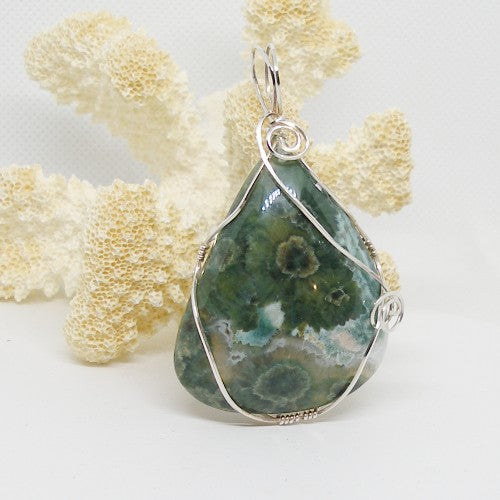 Teardrop-shaped green stone pendant with silver wire wrapping on a white background
