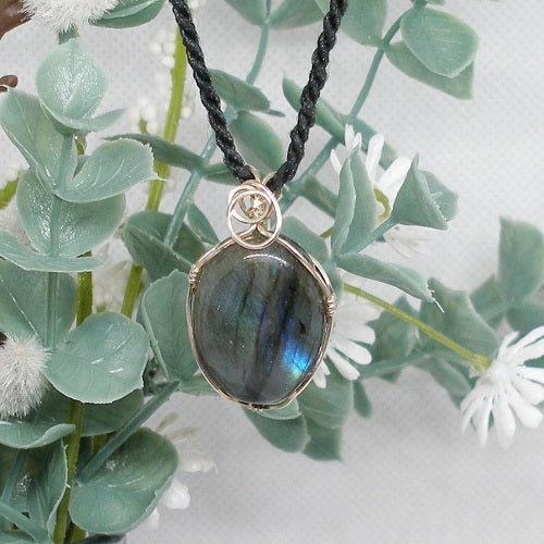 Necklace with a Labradorite pendant on a black cord, set against a soft white background with greenery.