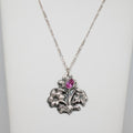 Silver necklace with floral pendant and pink gemstone on a white background