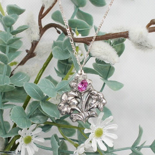 Silver necklace with a pink gemstone pendant on a branch with leaves and flowers