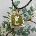 Necklace with a green cameo pendant featuring a classical design, surrounded by green leaves and white flowers.
