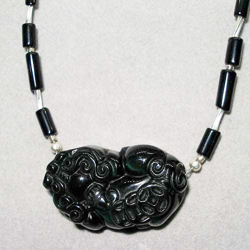 Necklace with black and silver beads and a detailed black dragon pendant on a light gray background