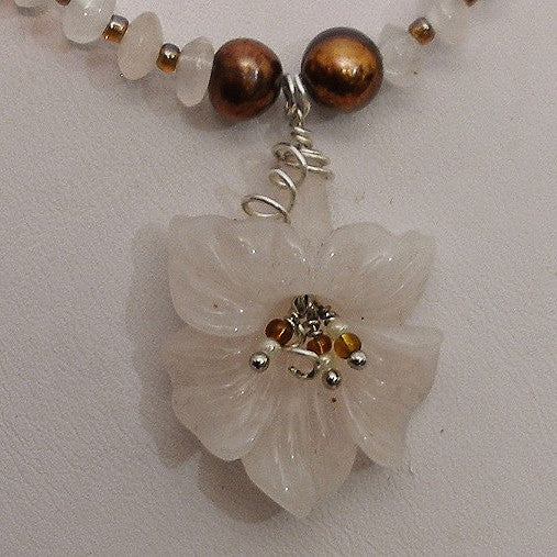Necklace with a white flower pendant and brown beads on a light gray background