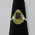 Ring with a pear-shaped yellow gemstone on a black stand against a gray background