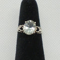 Silver ring with a large gemstone on a black stand against a gray background
