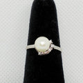 Pearl ring with crystal accents on a black stand against a gray background