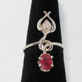 Silver ring with a red gemstone and zircon on a black stand against a white background