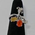 Silver ring with yellow and orang gemstones on a black stand against a gray background