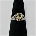 Silver ring with a yellow gemstone on a black velvet stand against a white background