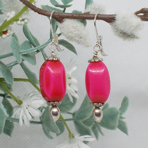 Pink beaded earrings with silver hooks on a branch with white flowers