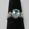 Silver ring with a blue gemstone on a black stand against a gray background