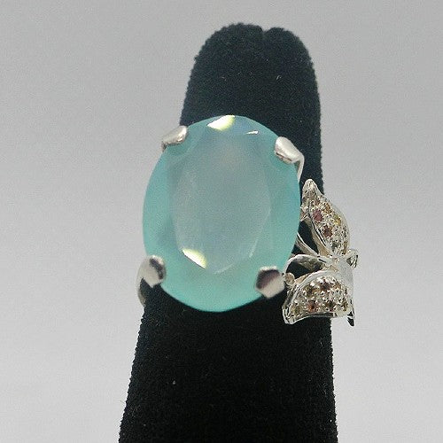 Ring with a blue gemstone and butterfly design on a black stand against a gray background