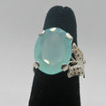 Ring with a blue gemstone and butterfly design on a black stand against a gray background