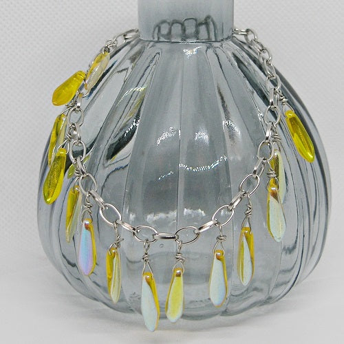Bracelet with iridescent yellow teardrop-shaped charms on a decorative glass bottle with  a light grey background
