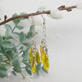 Yellow drop earrings hanging from a branch with a soft background