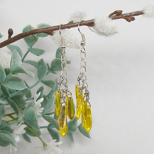 Yellow drop earrings hanging from a branch with a soft background